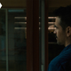 Colin farrell looks out a window in a blue shirt